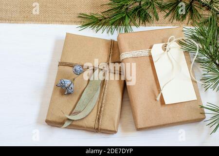 Handmade alternative Christmas gift boxes wrapped in grunge craft paper, christmas tree branches on the white background. Zero waste, plastic free, ca Stock Photo