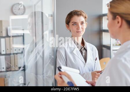 Waist up portrait of two female scientists writing on glass wall and holding clipboard while doing research in medical laboratory, copy space Stock Photo