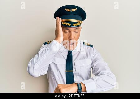 Handsome middle age mature man wearing airplane pilot uniform looking at the watch time worried, afraid of getting late Stock Photo