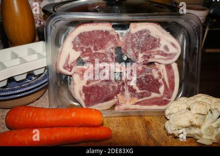 Raw lamb chops in tray with vegetables on kitchen chopping board Stock Photo