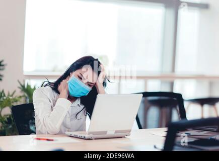 Stressed  and tired young  business woman wear face mask working on laptop Stock Photo