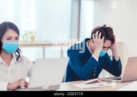 Stressed    business man wear face mask and  working on laptop in office Stock Photo