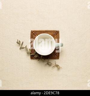 Empty mug cup with eucalyptus leaf on beige fabric background. top view Stock Photo
