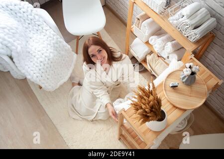 Young woman in warm robe is organizing linen closet with neatly folded towels, sheets and blankets. Stock Photo