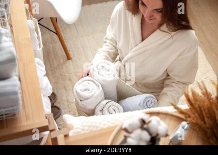 Young woman in warm robe is organizing linen closet with neatly folded towels, sheets and blankets. Stock Photo