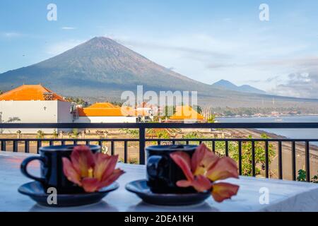 Two cups of coffee with flowers of Hibiscus Tiliaceus or Sea hibiscus, view of volcano Agung on the background. Amed, Karangasem, Bali, Indonesia. Stock Photo