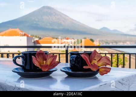 Two cups of coffee with flowers of Hibiscus Tiliaceus or Sea hibiscus, view of volcano Agung on the background. Amed, Karangasem, Bali, Indonesia. Stock Photo