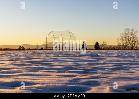Evening winter Coloradan landscape with baseball backstop, trees and the Rocky Mountains in the distance Stock Photo