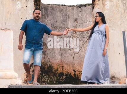 Two beautiful models, a young married couple, mother to be pregnant lady, holding hands, and looking at her husband standing portrait in front of ruin Stock Photo