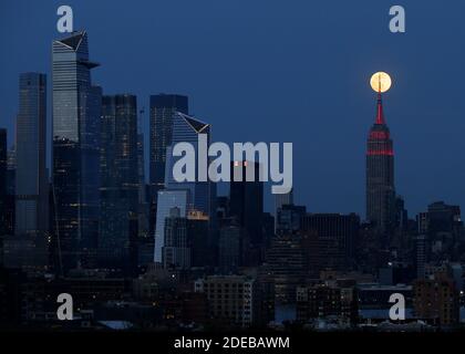 New York, United States. 29th Nov, 2020. A Pink Supermoon rises behind The Empire State Building and the Manhattan skyline with a light display lit in red to honor emergency workers fighting coronavirus on Tuesday, April 7, 2020. Throughout the COVID-19 battle, the signature white lights on the ESB have been replaced by the heartbeat of America, along with a white and red siren in the mast for heroic emergency workers on the front line of the fight.' Photo by John Angelillo/UPI Credit: UPI/Alamy Live News Stock Photo