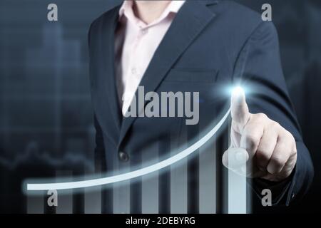 Businessman pointing arrow graph corporate future growth plan and increase percentage. Businessman Touching a Graph Indicating Growth on dark blue bac Stock Photo