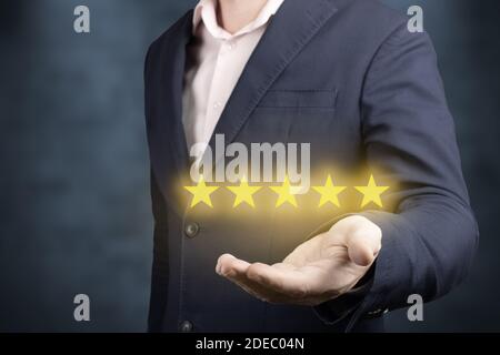 Businessman hand holding five stars on blue background. Businessman hand holding five stars. Rating 5 golden stars. Feedback, reputation and quality c Stock Photo