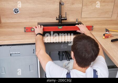 Male plumber installs a sink in the kitchen Stock Photo