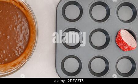 Chocolate muffins or chocolate cupcakes recipe. Chocolate batter in a bowl, and muffin pan with cupcake liners, close up view from above Stock Photo