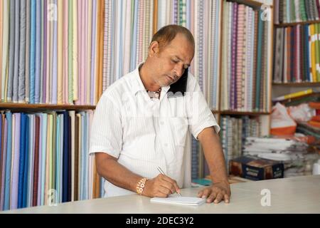 Shopkeeper taking order on mobile phone at cloth store - concept of small business owner noting down order, using technology and communication. Stock Photo