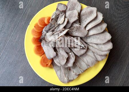 Slices of boiled tongue and carrot on yellow plate Stock Photo