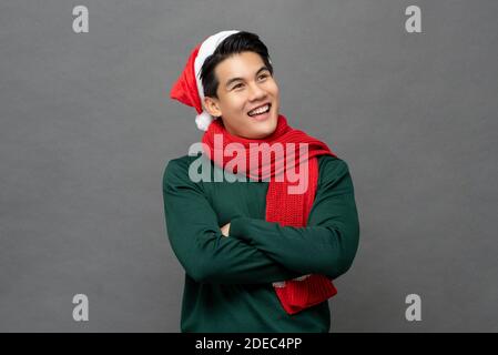 Smiling happy Asian man wearing colorful red and green Christmas theme clothes with arms crossed looking at copy space aside isolated on gray backgrou Stock Photo