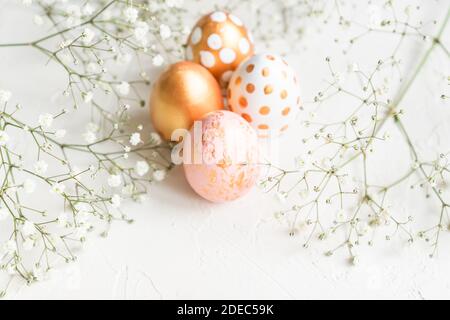 Colorful easter eggs painted in gold, white and pink colors on white background decorated with gypsophila flowers. Tender creative holiday background Stock Photo