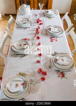 A top view of a Christmas table setting with vintage dishware, silverware and red decorations on white tablecloth - a Christmas concept Stock Photo
