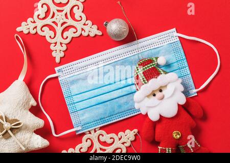 Christmas decorations and a medical mask on a red background, top view. Holidays quarantine concept due to covid-19 pandemic. Stock Photo