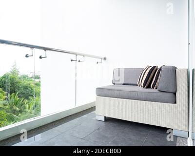 Comfortable rattan sofa bed with pillows decorated on balcony and patio on high building on white wall background near glass partition outside of the Stock Photo