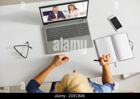 Senior woman sitting at table with laptop and having video call with her colleagues Stock Photo