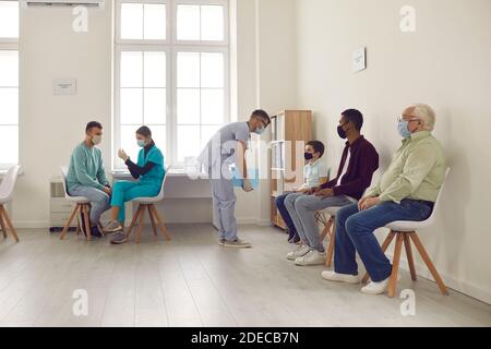 People in face masks waiting to get flu or Covid-19 vaccine sitting in hospital waiting-room Stock Photo