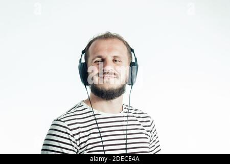 Smiling bearded happy man listens to music with big headphones. 30-35 years old. Isolated on white Stock Photo
