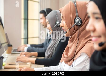 Asian muslim women wearing microphone headsets working as customer service operator team in call center office Stock Photo