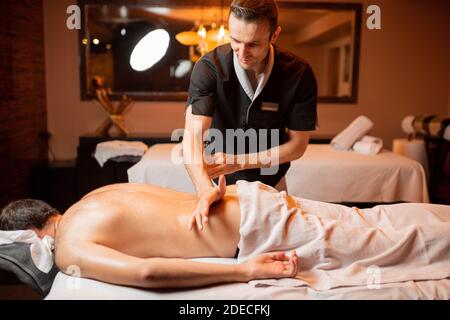 Professional masseur doing a deep back massage to a male client at Spa salon Stock Photo