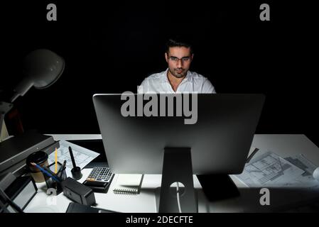 Dedicated Asian architect concentrating on working in front of computer at his desk late at night in the office Stock Photo