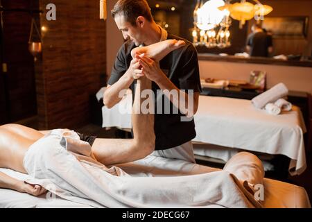 Professional therapist doing a deep massage to a male client at Spa salon. working on the lower body Stock Photo