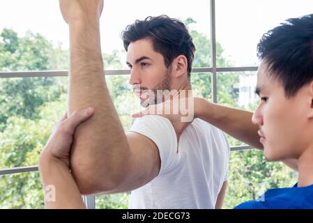 Physical therapist giving masssage and stretching athlete male patient shoulder and arm in clinic Stock Photo