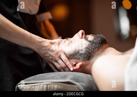 Bearded man receiving a facial massage, relaxing at Spa salon, close-up Stock Photo