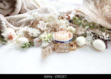 Spring still life with Easter eggs, candles in a pendant and flowers against the background of decor details. Easter holiday concept. Stock Photo