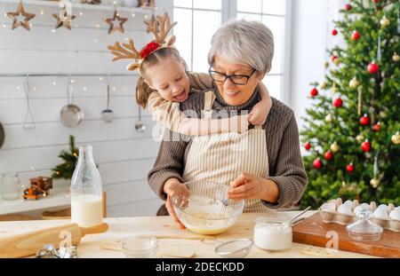 Merry Christmas and Happy Holidays. Family preparation holiday food. Grandma and granddaughter cooking cookies. Stock Photo