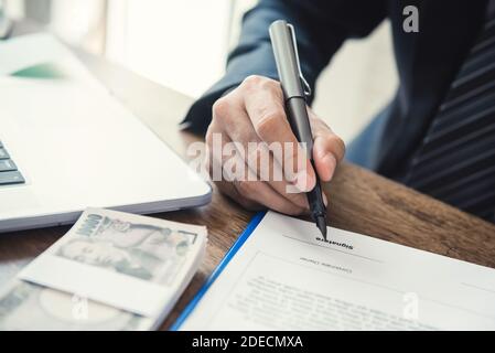 Businessman signing contract agreement of business loan with Japanese Yen banknote money at the table Stock Photo