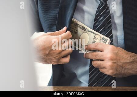 Rich businessman secretly keeping the Japanese Yen banknote money into his suit pocket, corruption concept Stock Photo