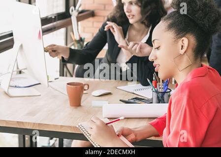Black businesswoman working with female office colleagues discussing project and taking notes at team meeting Stock Photo