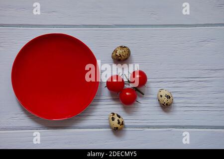 Red plate, cherry tomato and quail eggs on wooden background Stock Photo