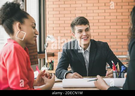 Young smiling businessman and black businesswoman  listening attentively to their colleague at finance meeting Stock Photo