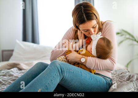 Mother and baby daughter plays, hugging, kissing at home. Happy family.