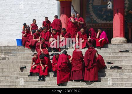 Xiahe, Gansu Province / China - April 28, 2017: Tibetan monks of the Gelug order gathering at the stairs of a building at Labrang Monastery. Some sitt Stock Photo