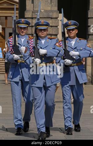 Three sentries of the Prague Castle Guard in their pale blue summer uniforms marching towards the viewer with shouldered rifles with bayonets fixed during a Changing of the Guard ceremony in the castle’s First Courtyard.   The sentries at the gates of the medieval castle change on the hour and there is also a daily 12 noon ceremonial Changing of the Guard, including a fanfare and a flag ceremony.  The castle is the official residence and office of the President of the Czech Republic or Czechia.