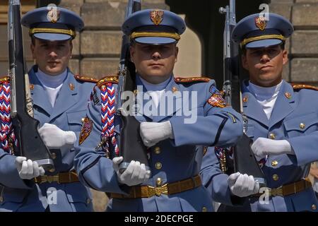 Three sentries of the Prague Castle Guard in their pale blue summer uniforms marching towards the viewer with shouldered rifles with bayonets fixed during a Changing of the Guard ceremony in the castle’s First Courtyard.   The sentries at the gates of the medieval castle change on the hour and there is also a daily 12 noon ceremonial Changing of the Guard, including a fanfare and a flag ceremony.  The castle is the official residence and office of the President of the Czech Republic or Czechia.