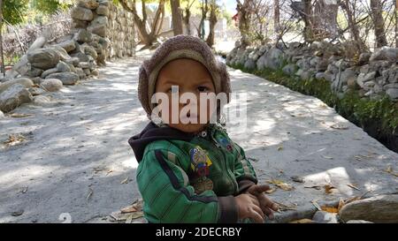 Kargil Jammu and Kashmir on 20 October 2018. A kids watching towards camera in kargil looking very innocent. Sits on road in sunny days with soft look Stock Photo