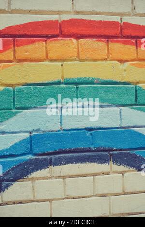 An image of the Rainbow flag painted on a brick wall in an urban location. Brick painted rainbow Stock Photo