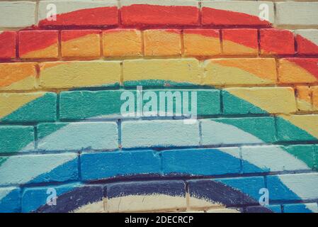 An image of the Rainbow flag painted on a brick wall in an urban location. Brick painted rainbow Stock Photo