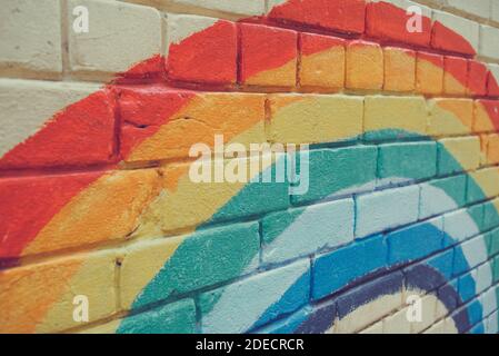 An image of the Rainbow flag painted on a brick wall in an urban location. Brick painted rainbow Stock Photo