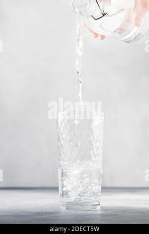 Clear water is poured from glass bottle into glass, gray background, selective focus Stock Photo